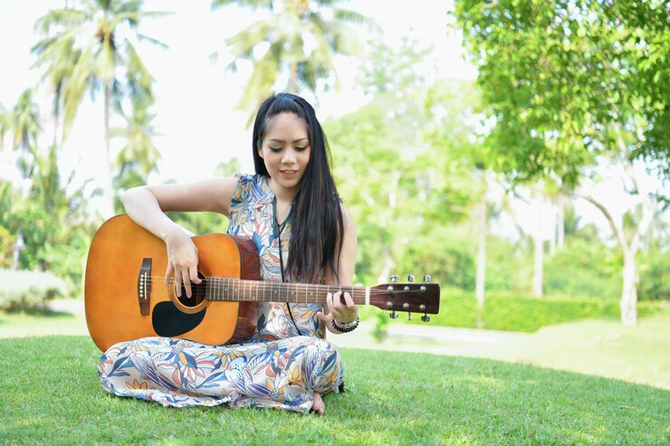 young-woman-playing-guitar-while-sitting-park_1048944-11674374